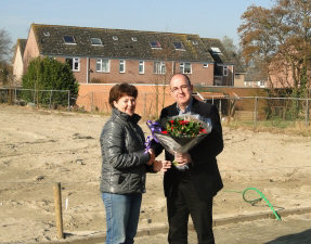 Mevrouw Van Geijstelen neemt bloemen en een kadobon in ontvangst van Peter Bevers, directeur R&B Wonen
